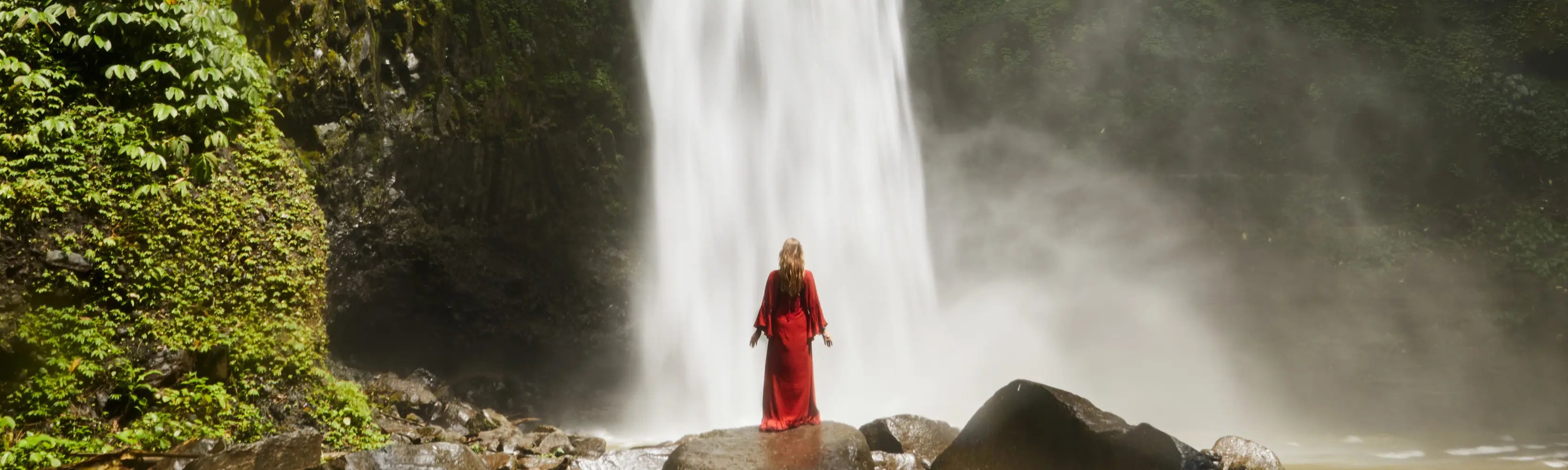 spray aurique cascade jungle bali femme en rouge sur rocher